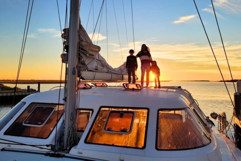 Young family raising the sail on the sailboat at sunset